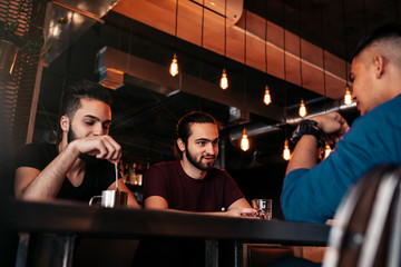 Group of mixed race young men talking and laughing in restaurant. Multiracial friends having fun in cafe. Guys hangout