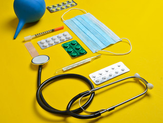 Medical equipment on a yellow background. Enema, blisters pills, notepad, stethoscope, syringe,...