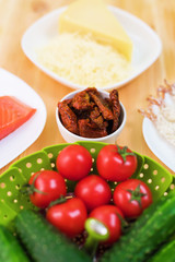 Still life of raw food in white plates on a wooden table. Frozen salmon on a plate next to cucumbers and tomatoes grated cheese and raw shrimps in breaded. Background for the theme of healthy eating