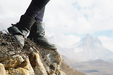 Close-up of female feet in vintage boots stand on a rock in the mountains against the background of...