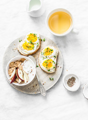 Morning breakfast table inspiration - sandwiches with cream cheese and boiled egg, yogurt with apple and flax seeds, herbal detox tea on light background, top view. Flat lay