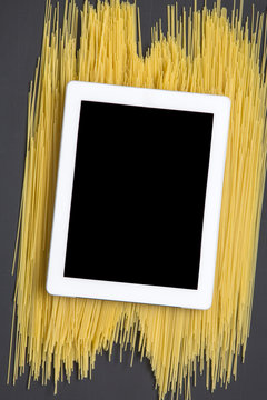Tablet on raw spaghetti. Dark background. Top view. Flat lay.