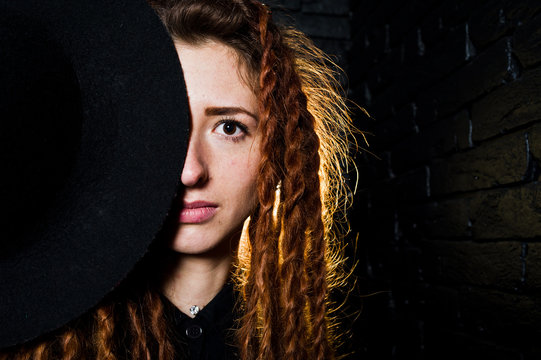 Studio shoot of girl in black with dreads and hat on brick background.