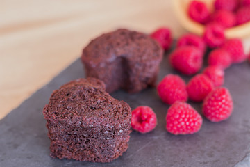 Two hearts of chocolate cake with raspberries on a slate.