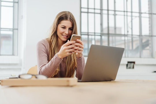 Young cheerful woman using phone at office