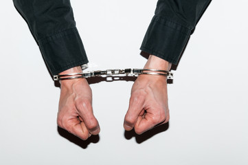 Handcuffed hands of arrested criminal man in handcuffs on table in police station