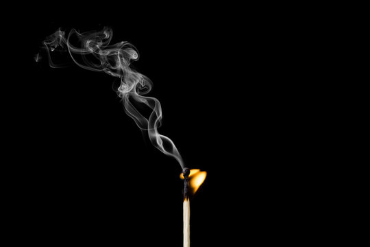 Matchstick burning with little flame and smoke on black background