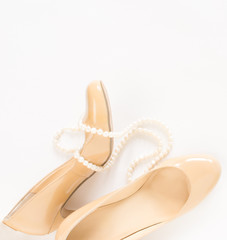Cream heeled women's shoes and pearls necklace on white background.