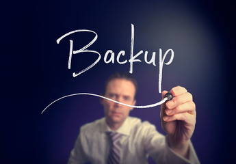 A businessman writing a Backup concept with a white pen on a clear screen.