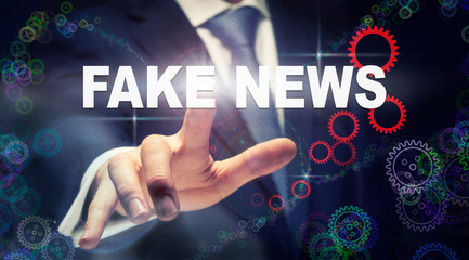 A businessman pressing a Fake News business concept on a graphical display of cogs