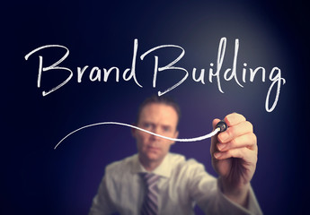 A businessman writing a Brand Building concept with a white pen on a clear screen.