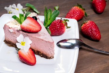 Strawberry cheesecake on black plate over rustic wooden background. Top view