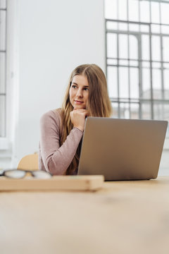 Young thoughtful woman sitting in front of laptop