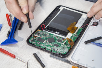 Dłonie pracownika serwisu elektronicznego rozkręcają uszkodzony tablet.