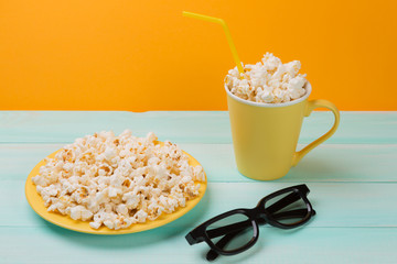 yellow plate and yellow cup with pop corn on turquoise boards and glasses for viewing 3d films, concept