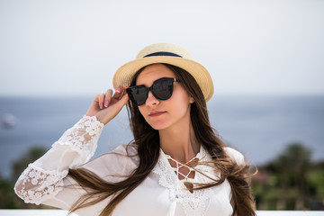 Portrait of a beautiful smiling young woman wearing straw hat and sunglasses while standing outdoor.