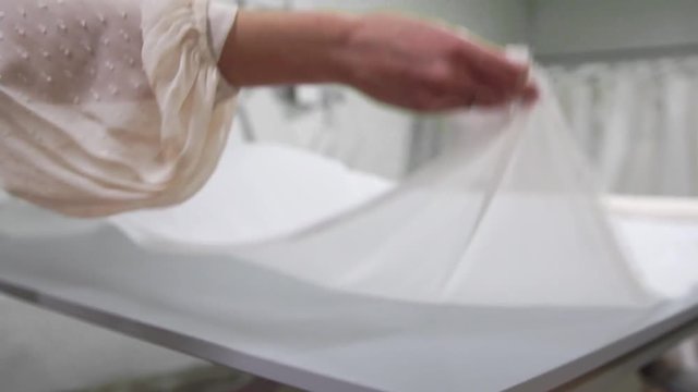 Clothing designer is working with measurements on a studio table. Shot on in 4K UHD . Closeup deploy a skein of white fabric in white and light-colored sewing in slow motion.