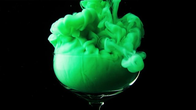 Beautiful glass goblet envelops thick green smoke. A magical and magical potion is poured into a glass vessel on a black background. Slow motion.