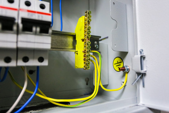 Electrical ground wires is connected to ground copper bar or earth bonding bar in metal electric breaker box with electrical circuit breakers and electrical grounding sign near ground bolt