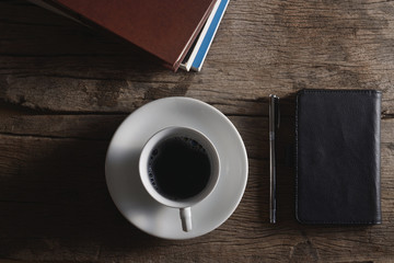 Book, pen, leather bag and coffee cup on wooden floor.