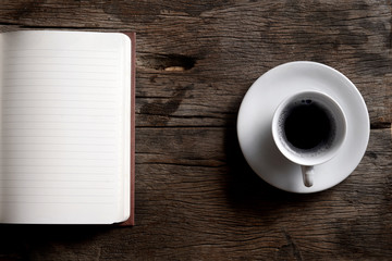 Open notebook with coffee cup on wooden table.