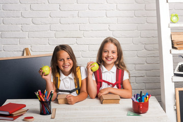 Little girls eat apple at lunch break. Friendship of small sisters in classroom at knowledge day. School time of girls. Happy school kids at lesson in september 1. Back to school and home schooling