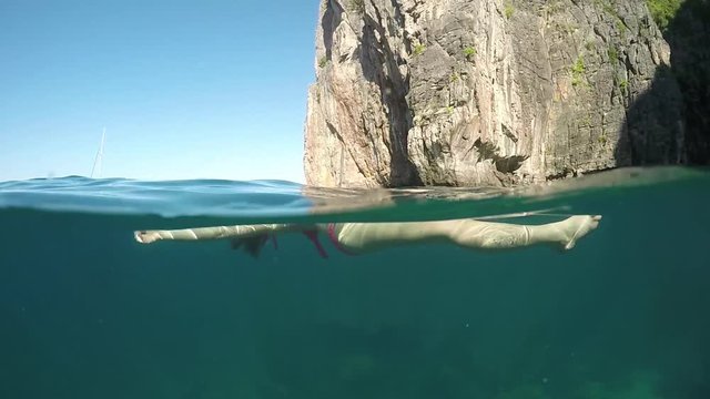 SLOW MOTION, HALF-HALF: Drowned young female's body floating on the surface of emerald ocean. Relaxed woman swims on her back and looks at the spectacular limestone cliffs near sunny Phi Phi Islands.