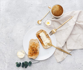 Toasted bread slices with adjacent butter and butter knife on rustic linen tablecloth. Top view,...