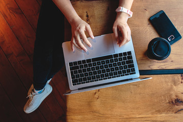 Overhead flat lay of laptop keyboard and coffee cup in cozy hipster cafe. Freelancer female hands typing on a netbook on wooden desk