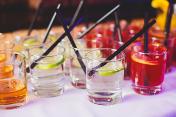 Beautiful row line of different colored alcohol cocktails on a party,  on decorated catering bouquet table
