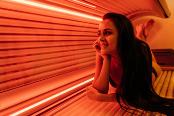 happy young woman sunbathing in a solarium under ultraviolet rays, wants a beautiful tanned skin