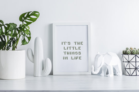 Creative desk with mock up white frame, cacti, elephant figure and plant. White wall background. Modern interior.