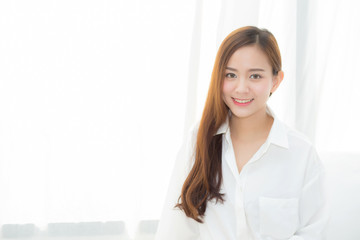 Portrait of beautiful young asian woman standing the window and smile while wake up with sunrise at morning, lifestyle and relax concept.