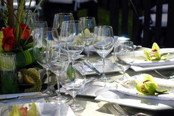 Wine glasses, silverware, plates, flowers making up the place settings at an outdoor catered party. 