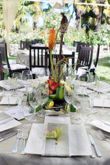Wine glasses, silverware, plates, flowers making up the place settings at an outdoor catered party. 