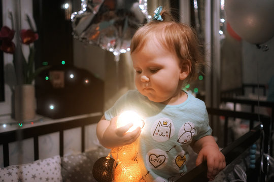 Cute child standing in the bed and playing with Christmas lights