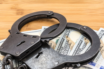 black metal handcuffs lying on the 100 dollars banknotes