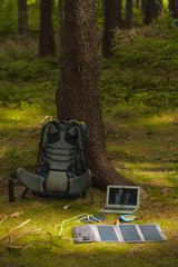 portable technology, solar panel, tablet, laptop and backpack in a forest