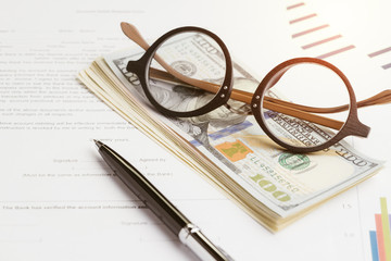 Buy and sell or leasing contract against bank, eyeglasses on pile of US dollar banknotes, printed paper form with pen to sign document with graph and price chart