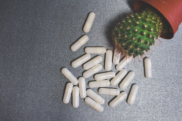 Top view of white capsules and a cactus with spines on a gray illuminated background. Drug interactions, adverse or side effects background or concept - obrazy, fototapety, plakaty