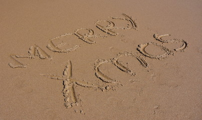 Merry Xmas written on sand at sunset. Merry Christmas lettering on the beach. 
