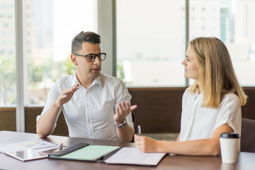 Serious CEO consulting female employee at meeting. Young Caucasian businessman wearing glasses...