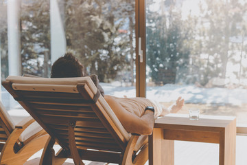 Man resting on wooden sofa in spa hotel. Man relaxing after hard day at spa salon with panoramic view.Sunligth wooden interior