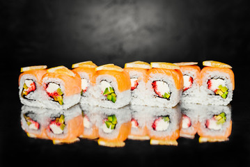 Roll Philadelphia on black background made of smoked salmon, nori, pickled rice, philadelphia cheese, masago caviar, avocado, lemon. Traditional Japanese cuisine. Sushi menu. Japanese food. Free-space