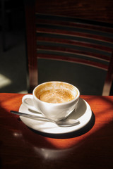 half empty cup of cappuccino coffee in a hard sunlight