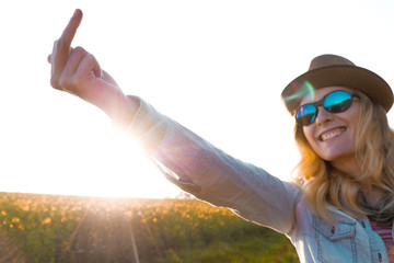 portrait of a young caucasian woman wearing a stylish hat and sunglasses standing outdoors and showing a middle finger