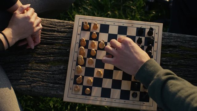 Top down shot of a young couple playing chess outdoors on a wooden bench