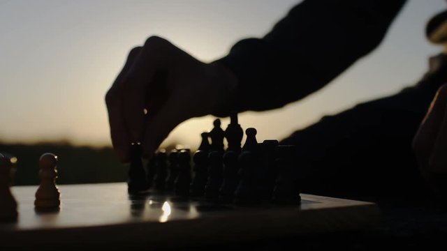 Close up of male and female hands playing chess outdoors in the sunlight, in slow motion