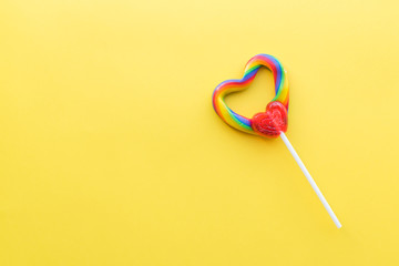 Single heart-shaped lollipop with rainbow swirl colors with bright yellow background