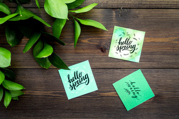 Spring lettering, spring motto. Lettering hello spring on stickers among green foliages on dark wooden table top view